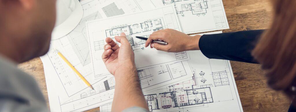 2 Menschen zeigen auf einen sehr strukturierten Bauplan eines Hauses 